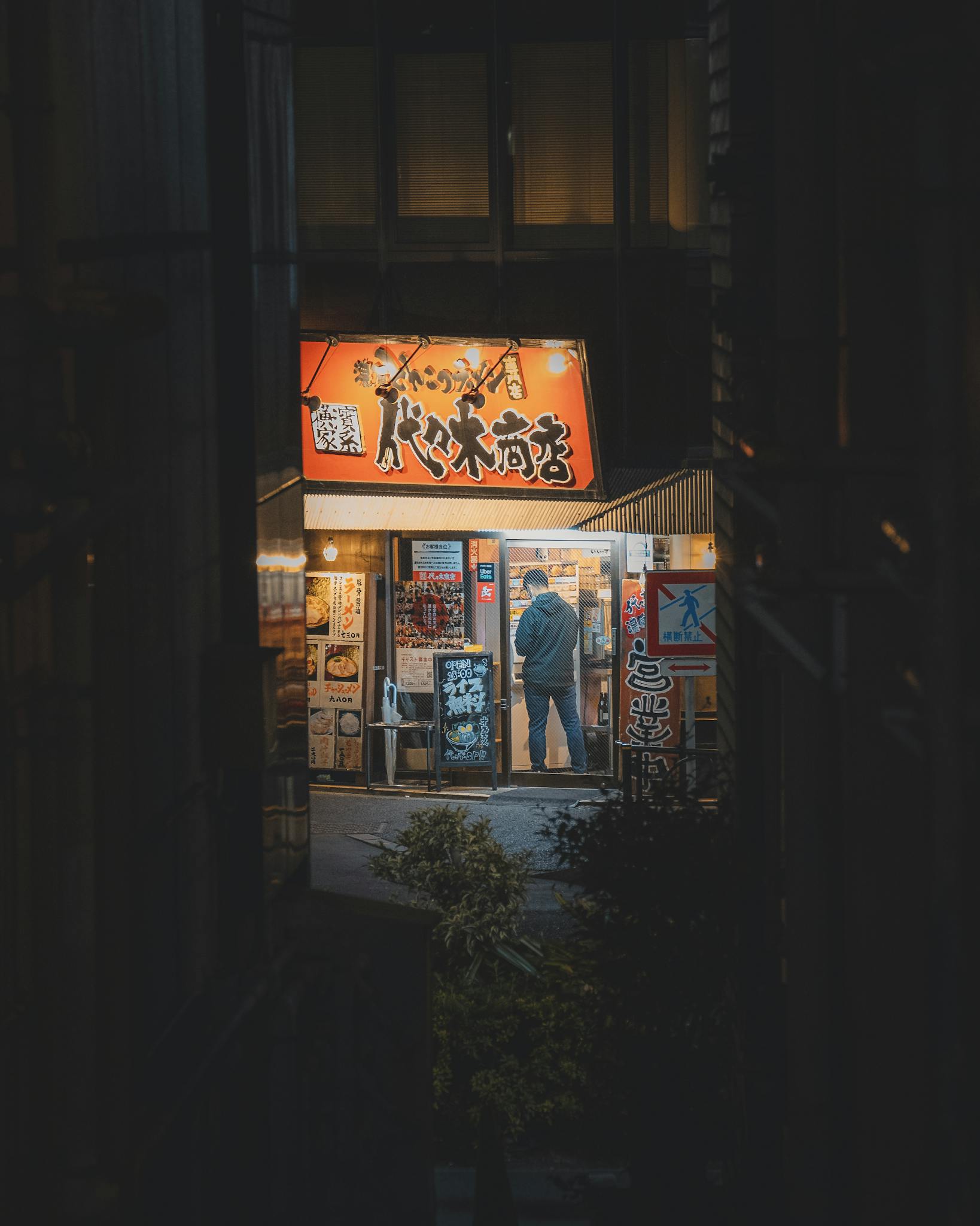 A person stands inside an illuminated street restaurant in Shinjuku City, Tokyo, Japan at night.